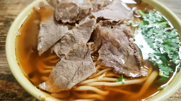 Büyük bir kase sığır etli şehriye çorbası ve taze yeşil kişniş ve ahşap bir masa..