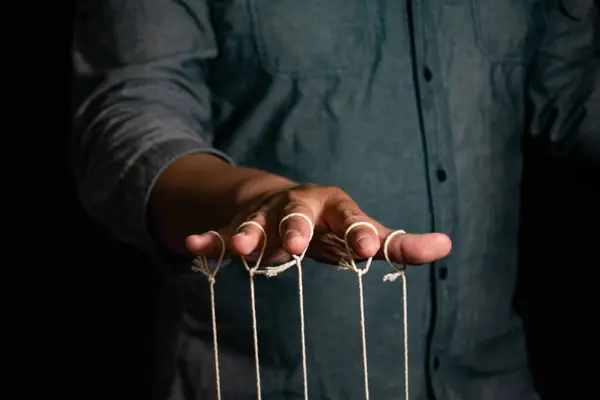 İnsan 'ın Yakın Çekimi Kuklayı Parmaklarıyla Kontrol Ediyor. Man 's Hand, parmakları siyah arkaplan ve manipülasyon konseptine bağlı olan kuklayı kontrol eder.