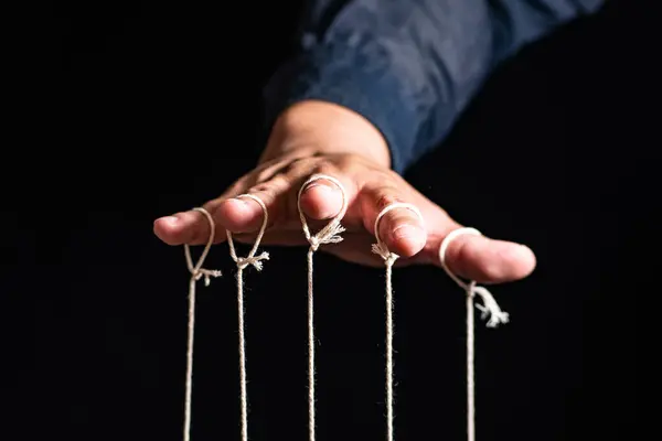 İnsan 'ın Yakın Çekimi Kuklayı Parmaklarıyla Kontrol Ediyor. Man 's Hand, parmakları siyah arkaplan ve manipülasyon konseptine bağlı olan kuklayı kontrol eder.