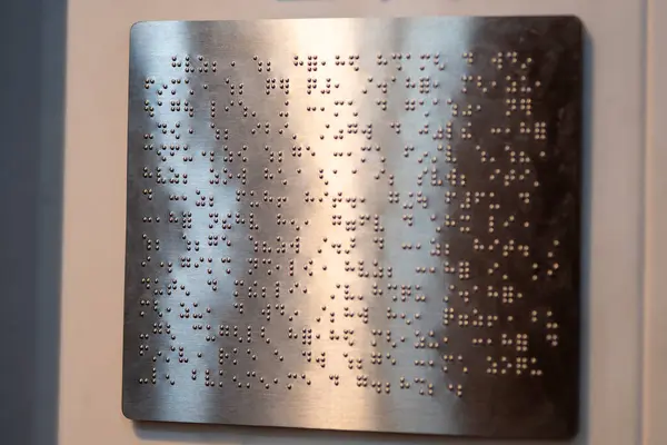 Yakından, desenli, metalik bir yüzey üzerindeki eğimli bir ışıkla aydınlatılmış altın kabartma alfabeyle yazılmış bir fotoğraf..