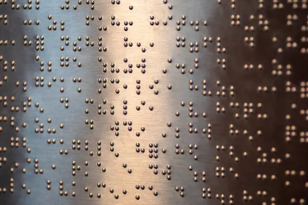 Yakından, desenli, metalik bir yüzey üzerindeki eğimli bir ışıkla aydınlatılmış altın kabartma alfabeyle yazılmış bir fotoğraf..