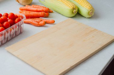 Taze organik mısır, taze havuç ve vişneli domateslerle çevrili boş bir bambu kesme tahtasının yakın çekimi sağlıklı yemek ve yemekler için hazırlanıyor..