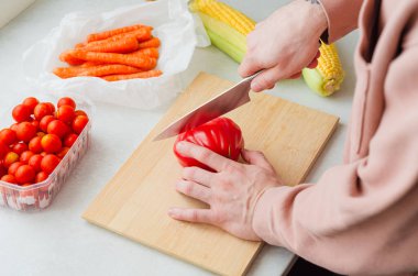 Pirzola bifteği domatesini mısır, taze havuç ve vişneli domates gibi mevsimlik organik sebzelerle doğrayan bir adamın yakın çekimi.. 