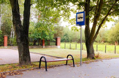 Otobüs durağında bir bank ve Polonya 'nın Masovia bölgesinde bir ağacın yanında işaret levhası var. Manzaralı kırsal ortam seyahat, ulaşım ve açık hava yaşam tarzı kavramları için ideal.