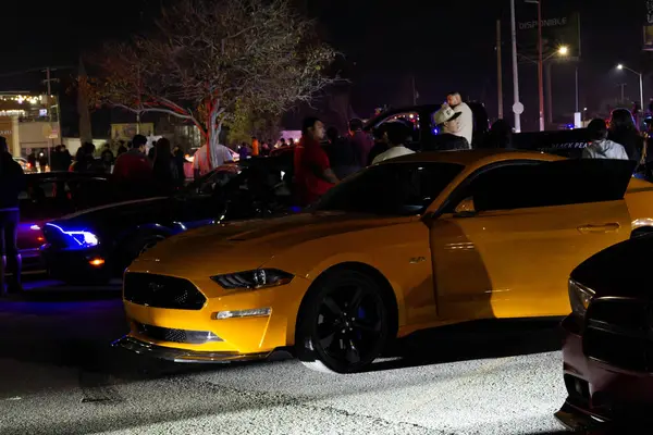 Otoparkta araba toplantısı sırasında düşük ışık alan sarı bir mustang.