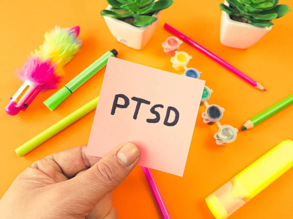 PTSD acronym Post Traumatic Stress Disorder handwritten on sticky note with colorful child supplies. Mental health disorder concept