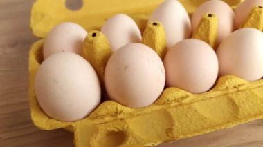 Tahta arka planda sarı kağıt sandıkta beyaz tavuk yumurtası.