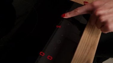 A woman's hand turns on an induction hob. Cooking. Touch panel induction furnace, modern appliance
