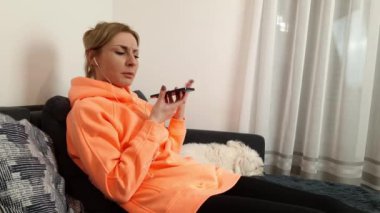 Parlak turuncu bluz giyen, kulaklık takan ve akıllı telefondan konuşan beyaz bir kadın. Arkadaşla sohbet, dedikodu, eğlence konsepti.