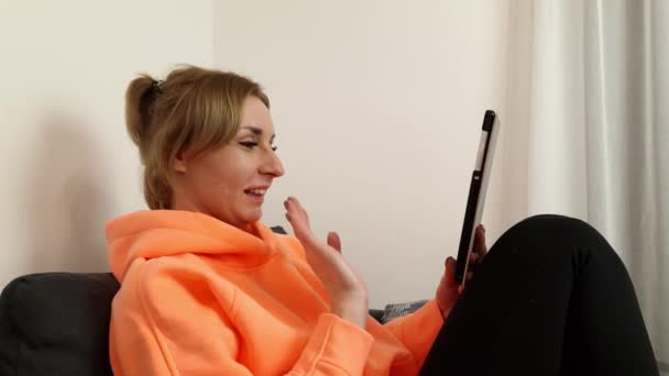 Jovem Mulher Sentada Sofá Olhando Para Tela Tablet Acenando Mão — Vídeo de Stock