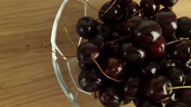 Olgun kirazlar cam kasede, ahşap arka planda, yakın plan.