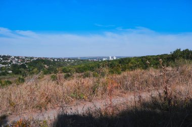 Panoramic view of Tonelna Balka in Dnipro, Ukraine, captured on September 16, 2025. Dry autumn grass, green trees and city skyline under a bright blue sky create a natural urban landscape.