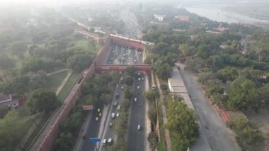 Aerial Drone shot of a Indian railways train crossing a bridge over a busy road next to Red Fort Yamuna River in New Delhi India 