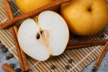 Tarçın çubukları ve bambu hasırının üzerindeki tüm baharatla çevrili bir Asya armudunun yakın çekimi. Zengin dokular ve ılık sonbahar tonları Chuseok hasadını ve Kore Şükran Günü geleneklerini çağrıştırıyor..