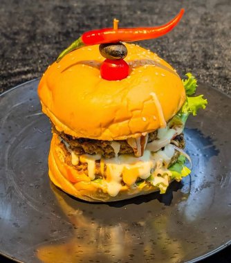 Close-up of a juicy cheeseburger with crispy bacon, grilled beef patty, melted cheese, and sesame seed bun, topped with creamy sauce. Perfect fast food concept on a plate.