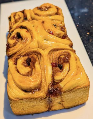 Close-up of freshly baked cinnamon rolls topped with colorful dried fruits and glazed for a shiny finish.