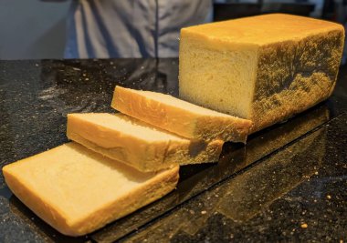 Close-up of freshly baked bread loaf with sesame seeds on top, sliced and displayed on a dark surface.