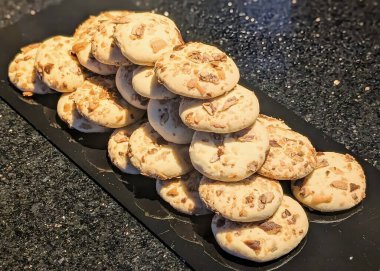 A close-up view of freshly baked almond cookies stacked neatly on a dark stone surface.
