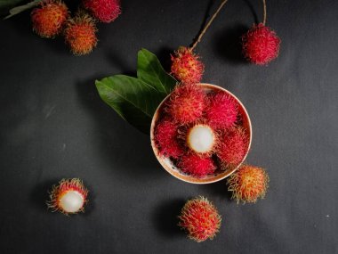 Bir yığın Rambutan meyvesi siyah arka planda beyaz bir kasede ve tahtada birkaç yeşil yaprak var. Tropikal meyve. Rambutan 'ın tatlı meyveleri