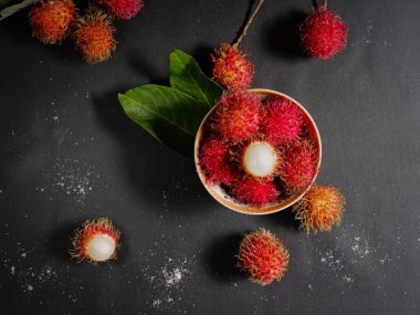 Bir yığın Rambutan meyvesi siyah arka planda beyaz bir kasede ve tahtada birkaç yeşil yaprak var. Tropikal meyve. Rambutan 'ın tatlı meyveleri