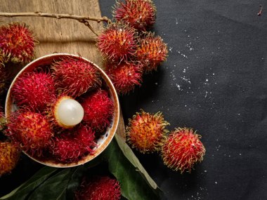 Bir yığın Rambutan meyvesi siyah arka planda beyaz bir kasede ve tahtada birkaç yeşil yaprak var. Tropikal meyve. Rambutan 'ın tatlı meyveleri