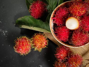 Bir yığın Rambutan meyvesi siyah arka planda beyaz bir kasede ve tahtada birkaç yeşil yaprak var. Tropikal meyve. Rambutan 'ın tatlı meyveleri