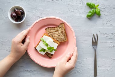 Sağlıklı atıştırmalık konsepti. Ekmek ve zeytinli keçi peyniri, üst manzara. Kadın elleri plakayı tutsun, gri mermer arka plan. 