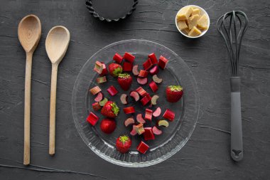 Siyah arka planda meyveli tart hazırlığı. Fırın aletleri, tereyağı ve raventli gezginler, üst manzara.. 