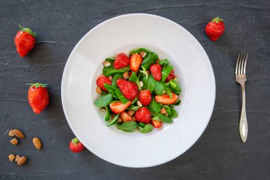 Healthy salad with nuts and berries on black table, top view. 