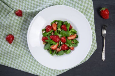 Tasty strawberry salad with nuts and rocked salad on black background, top view. 