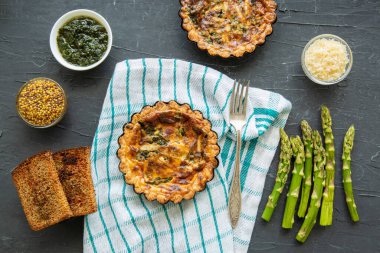 Tasty summer tart with asparagus, vegetables, grilled bread and spices on kitchen towel on black background, top view. 