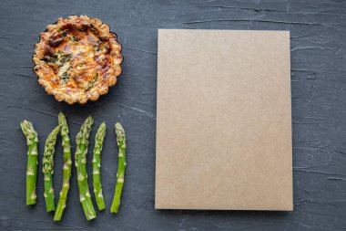 Little tart or quiche with asparagus on black marble background, space for text and recipe, copy space, top view. 