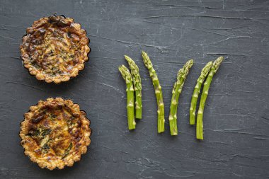 Vegetarian asparagus quiche or tart on black background, healthy summer snack, top view. 