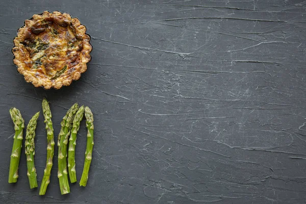 Little tart or quiche with asparagus on black marble background, space for text and recipe, copy space, top view.