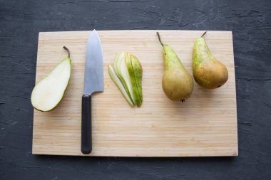 Pear slices on wooden cutting board on black background, top view. Summer dessert preparation. 
