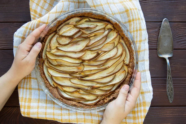 Female hands hold baked pear pie on rustic wooden table, vintage style, top view.