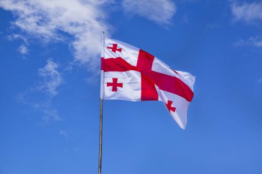 Gürcistan bayrağı parlak mavi arka planda dalgalanıyor. 