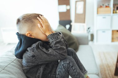 Depresyondaki üzgün çocuk evde, yatakta oturuyor. Küçük çocuk kafasını ellerinin arasında saklıyor. Kafası karışık sorunlu çocuk, çocukluk kabadayılığı, depresyon stresi veya hüsran konsepti