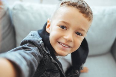 Çocuğun fotoğrafı akıllı telefonla selfie çekiyor. Sağlıklı dişleri olan mutlu küçük çocuk selfie çekiyor. Çocuğun fotoğrafı kapalı mekanda akıllı telefonlu selfie çekiyor. Çocuk selfie çekiyor.. 