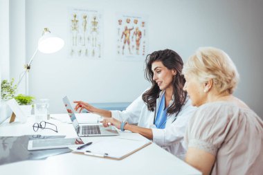 Doktor ve bayan hasta hastanede masada oturmuş dizüstü bilgisayara bakıyorlar.