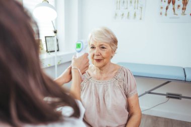 Doktor ve yaşlı kadın klinikte sıcaklık ölçüyorlar.