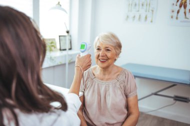 Doktor ve yaşlı kadın klinikte sıcaklık ölçüyorlar.