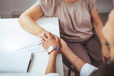 Klinikteki kıdemli hastasının elini tutan doktor.