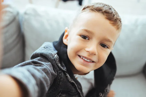 stock image Cute little boy taking selfie on light background. Happy little boy with healthy teeth taking selfie. Photo of boy takes selfie with smart phone indoors. Boy takes selfie