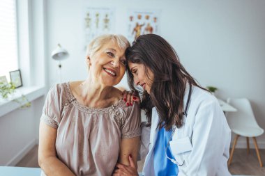 Neşeli ve arkadaş canlısı gülümseyen kadın bir doktor ve klinikteki kıdemli bir hastanın portresi.