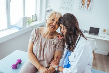 Neşeli ve arkadaş canlısı gülümseyen kadın bir doktor ve klinikteki kıdemli bir hastanın portresi.