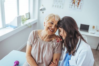 Neşeli ve arkadaş canlısı gülümseyen kadın bir doktor ve klinikteki kıdemli bir hastanın portresi.