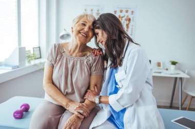 Neşeli ve arkadaş canlısı gülümseyen kadın bir doktor ve klinikteki kıdemli bir hastanın portresi.