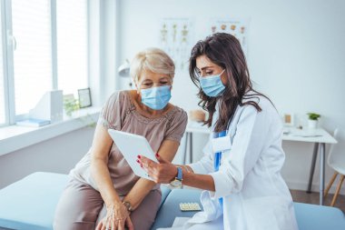 Kadın doktor ve kıdemli hastası tablet bilgisayara bakıyor.