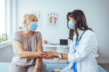 Klinikteki yaşlı hastasının elini tutan genç bayan doktor.